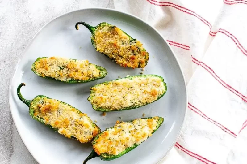 cinco jalapeno poppers de la freidora de aire cocinados y en un plato blanco con una servilleta blanca con rayas rojas a la izquierda. Todo sobre un fondo blanco.