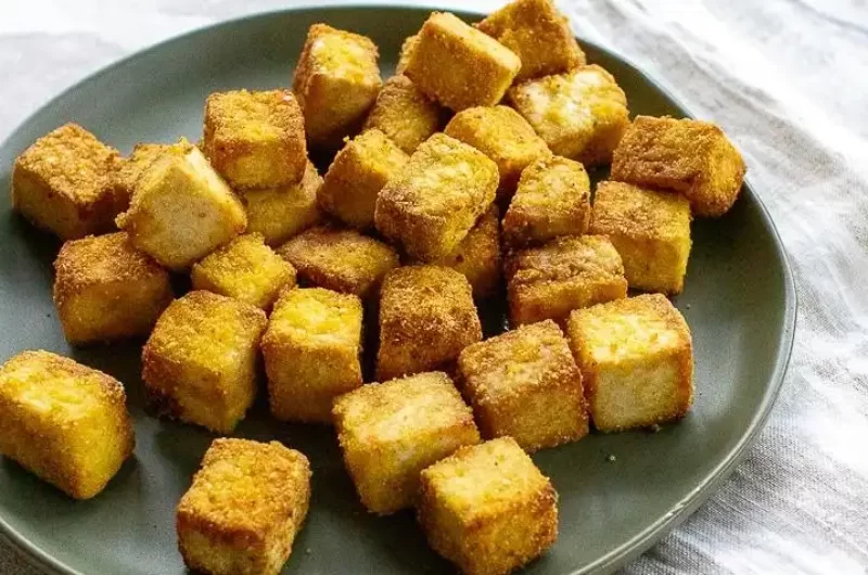 cubos de tofu cocidos de color marrón claro en un plato gris