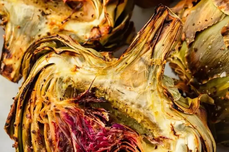 un primer plano de mitades de alcachofas asadas en un plato.