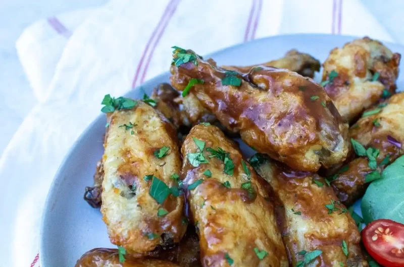 Un montón de trozos de alas de pollo a la barbacoa glaseados con una salsa marrón y cubiertos con trozos picados de perejil verde brillante